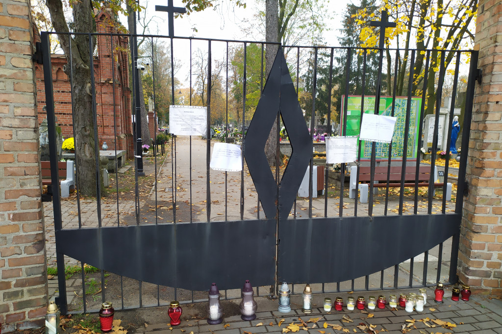 Znicze i kwiaty pod zamkniętymi bramami cmentarza