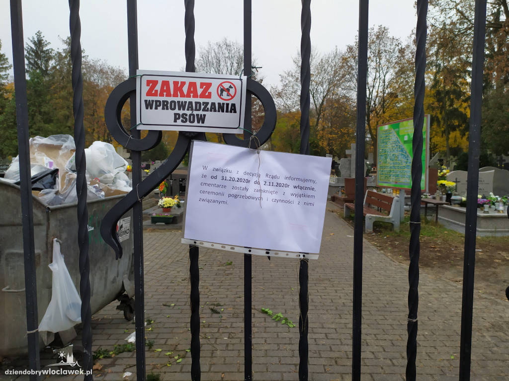 Znicze i kwiaty pod zamkniętymi bramami cmentarza
